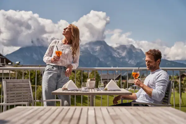 Ein Mann und eine Frau trinken aus einem Glas auf einem Balkon.