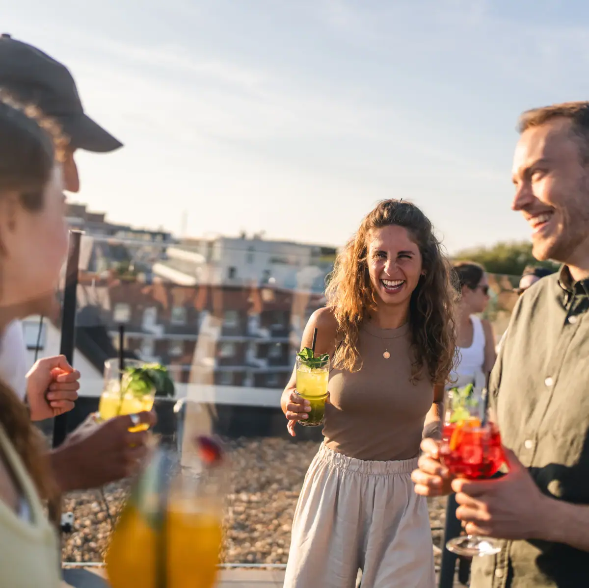 Gruppe von feiernden Menschen steht mit Cocktails auf einer Dachterrasse