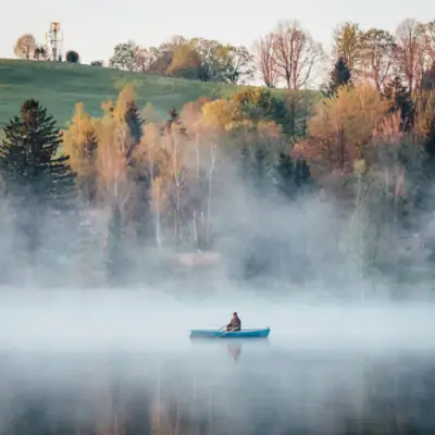 Eine Person in einem Boot auf einem nebligen See.
