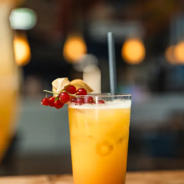 Ein Glas mit orangenem Drink, Strohhalm und Beeren.