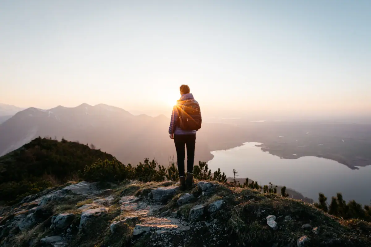 Wandern Garmisch-Partenkirchen Eine Person steht auf einem Hügel und blickt in die Sonne.