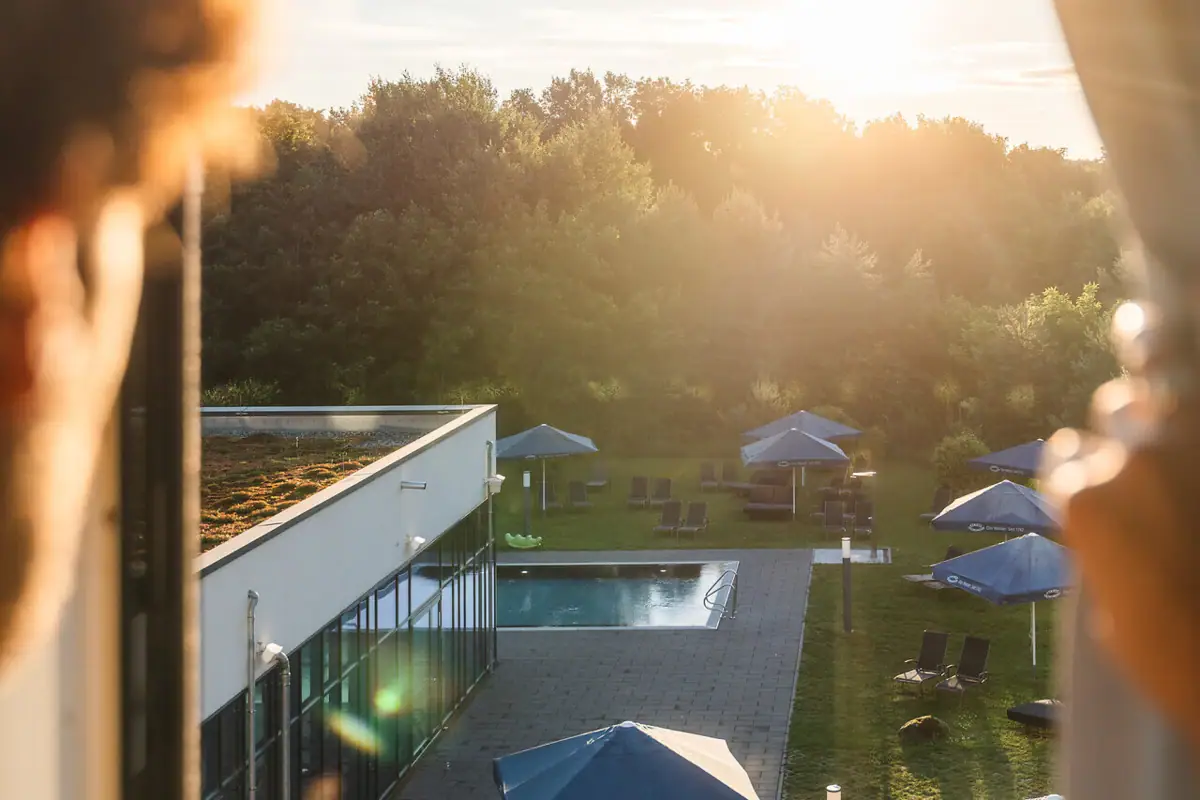 Eine Person blickt aus einem Fenster auf einen Pool mit Sonnenschirmen.
