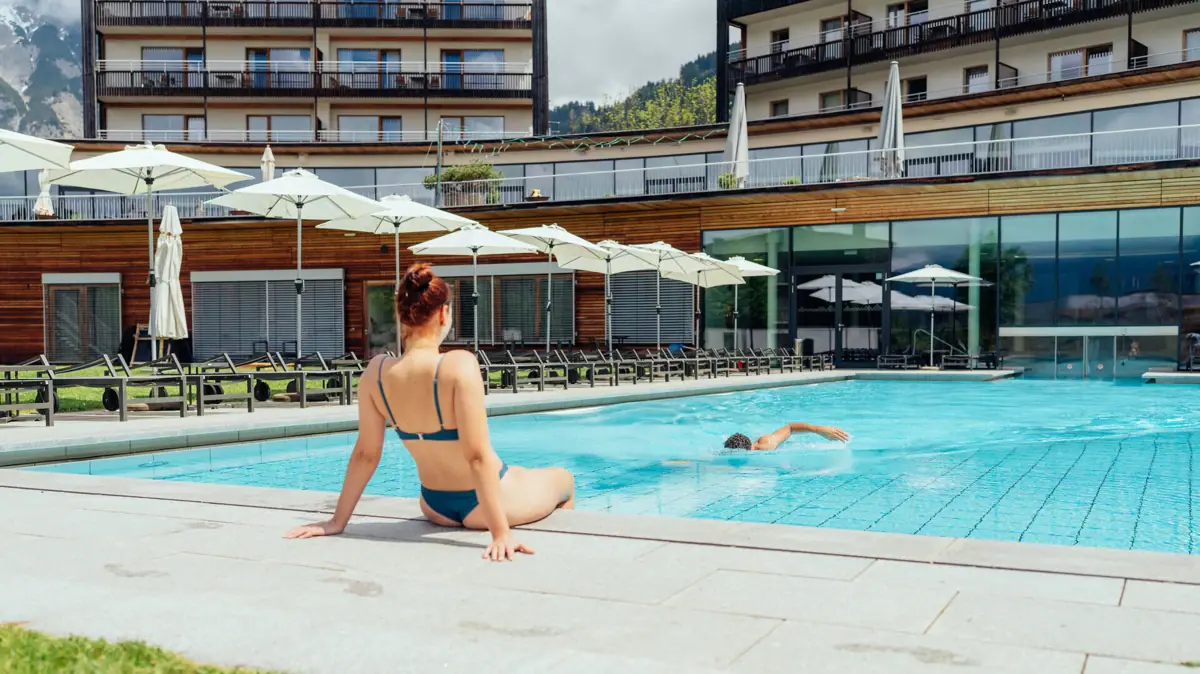 Außenpool Eine Frau sitzt in einem Pool, während ein Mann darin schwimmt.