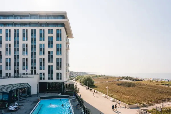 Hotel aja Warnemünde Ein Gebäude mit einem Pool und vorbeigehenden Personen.