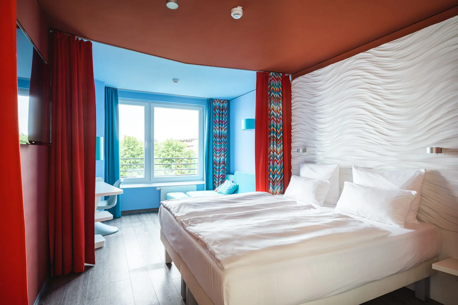 Ein Zimmer mit zwei Betten und roten Vorhängen vor einem Fenster im Hintergrund