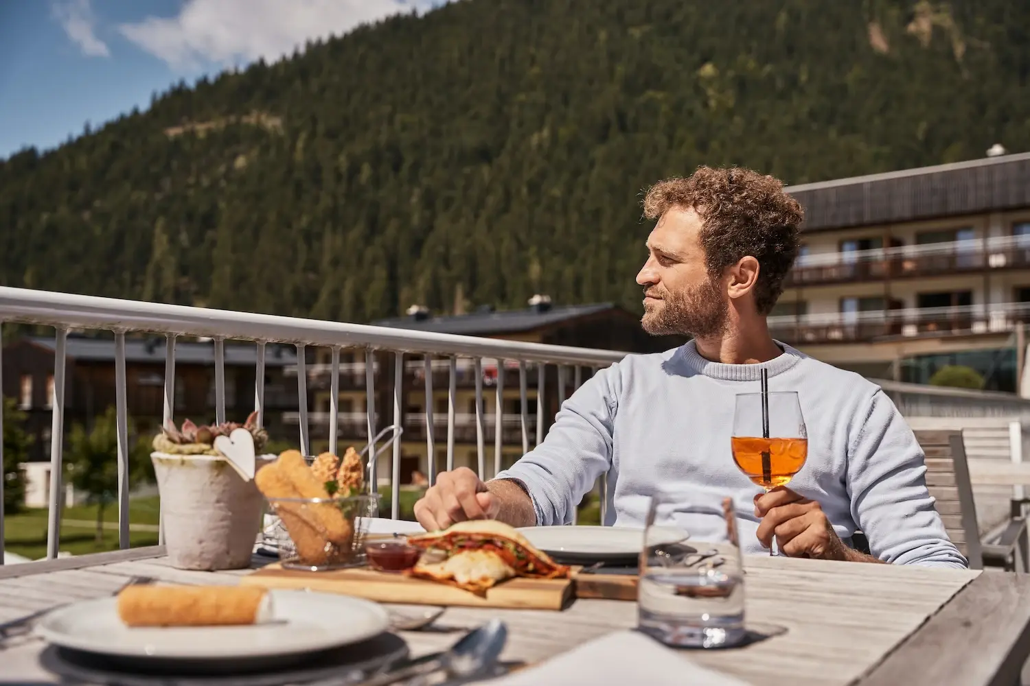 Mann sitzt an einem Tisch im Freien, umgeben von Speisen und Getränken.