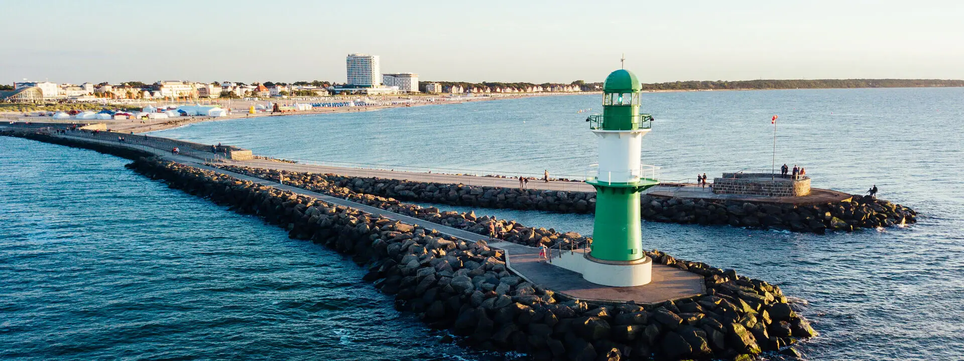 Grüner und weißer Leuchtturm auf Felsen im Wasser.
