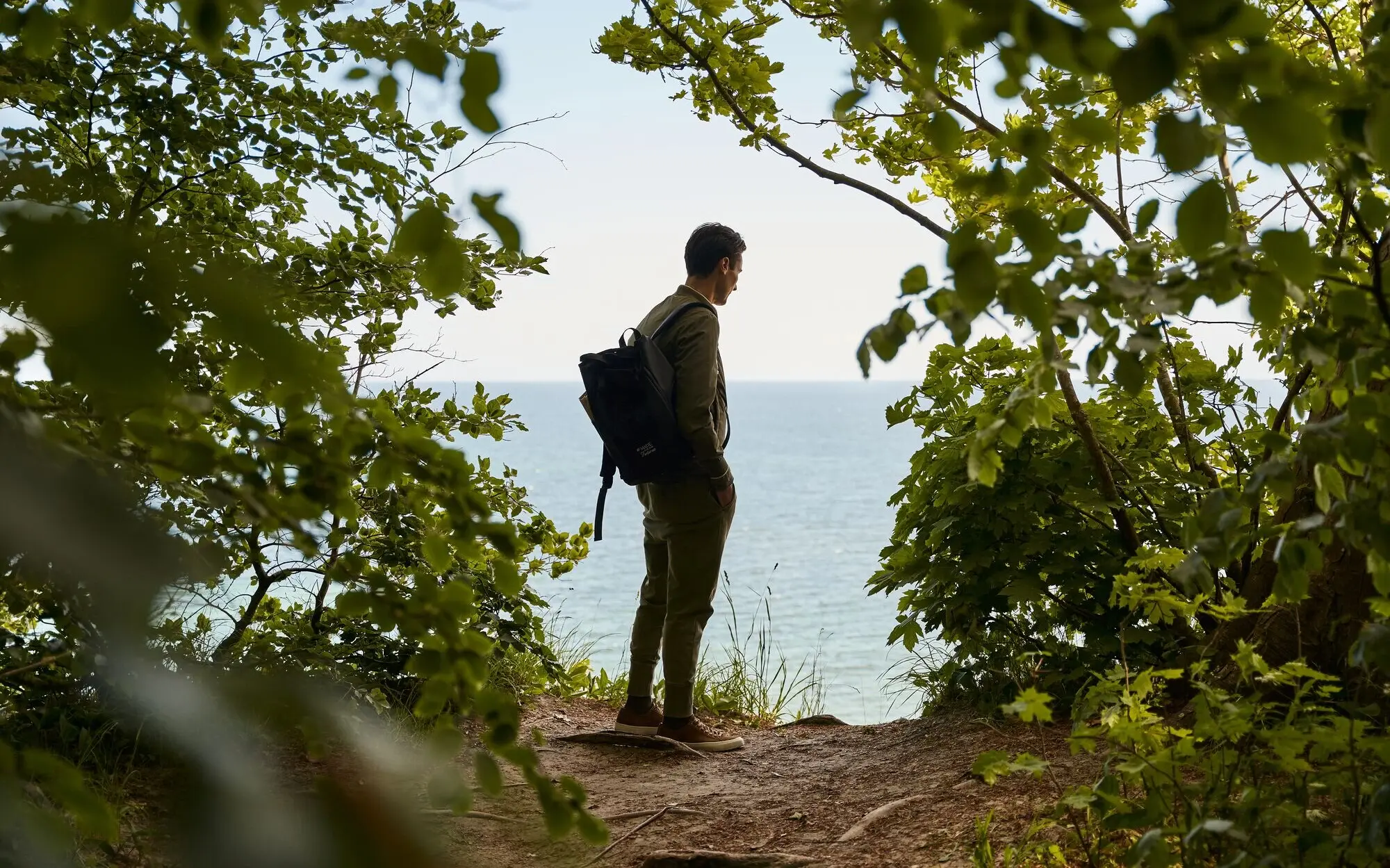 Ein Mann mit Rucksack steht auf einem Hügel im Freien.