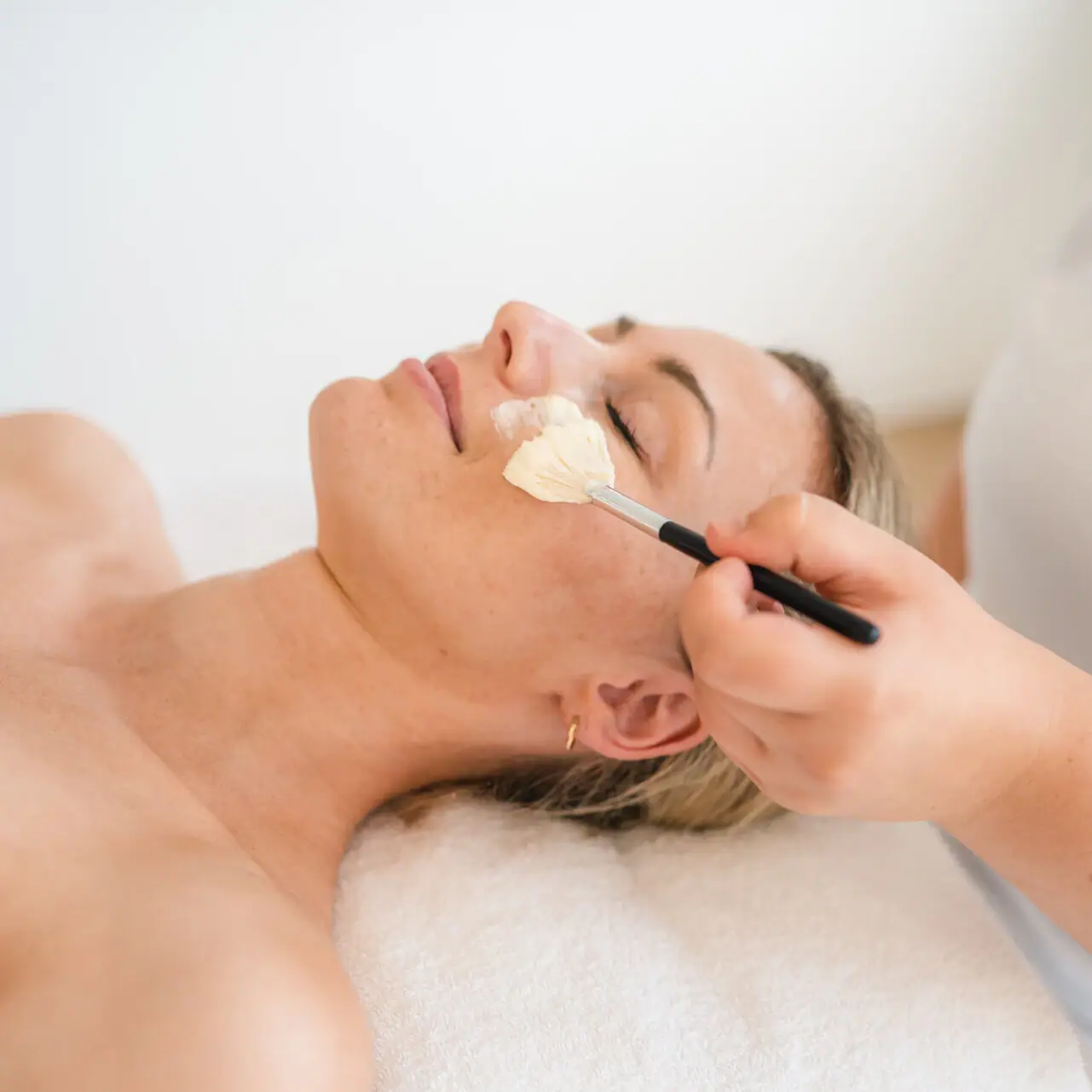Anwendungen im aja Warnemünde Eine Frau liegt mit einem Pinsel im Gesicht auf der Liege.
