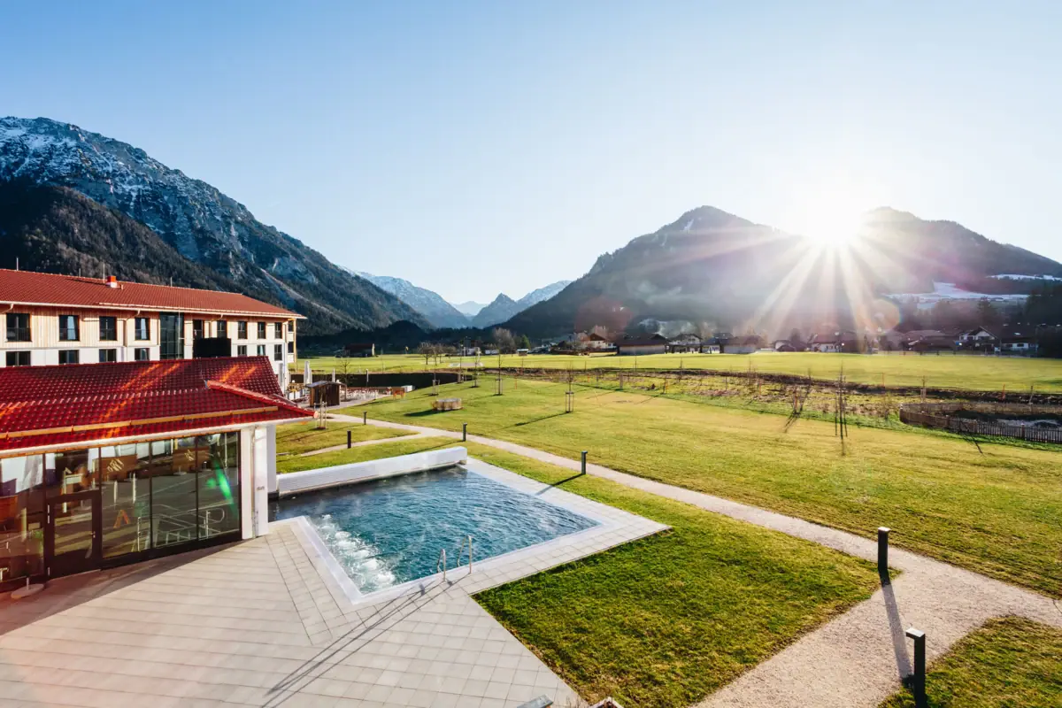 Der Outdoor Swimmingpool vom aja Ruhpolding mit dem Golfplatz und Bergen im Hintergrund.