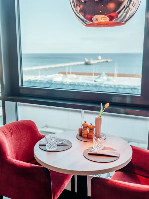 Ausblick aus dem JEDERMANNS Restaurant Grömitz Ein Tisch mit roten Stühlen und einer roten Lampe.