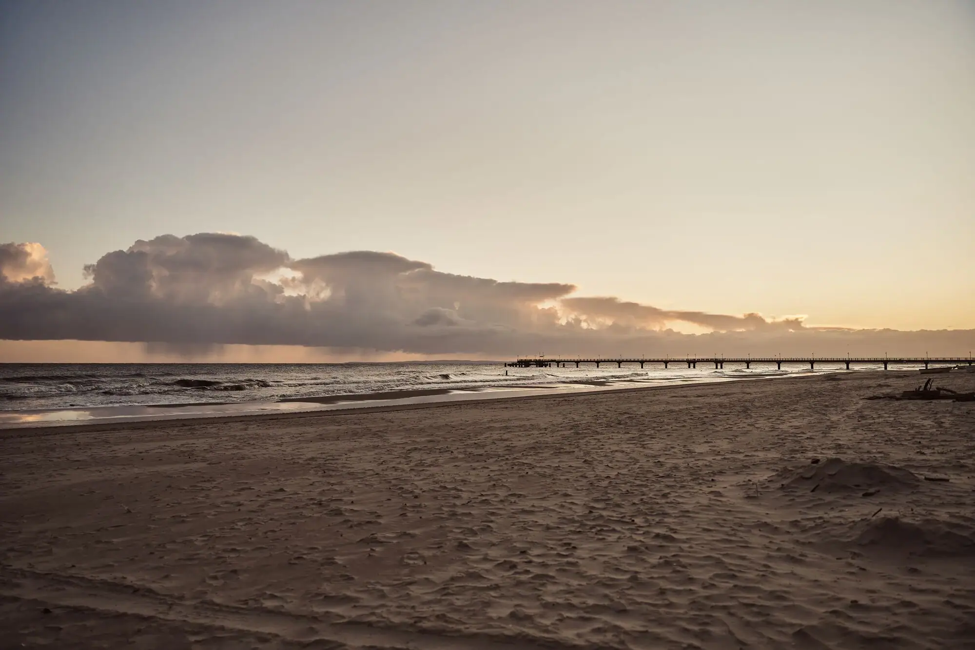 Ein Strand mit einem Pier und Wasser im Vordergrund.