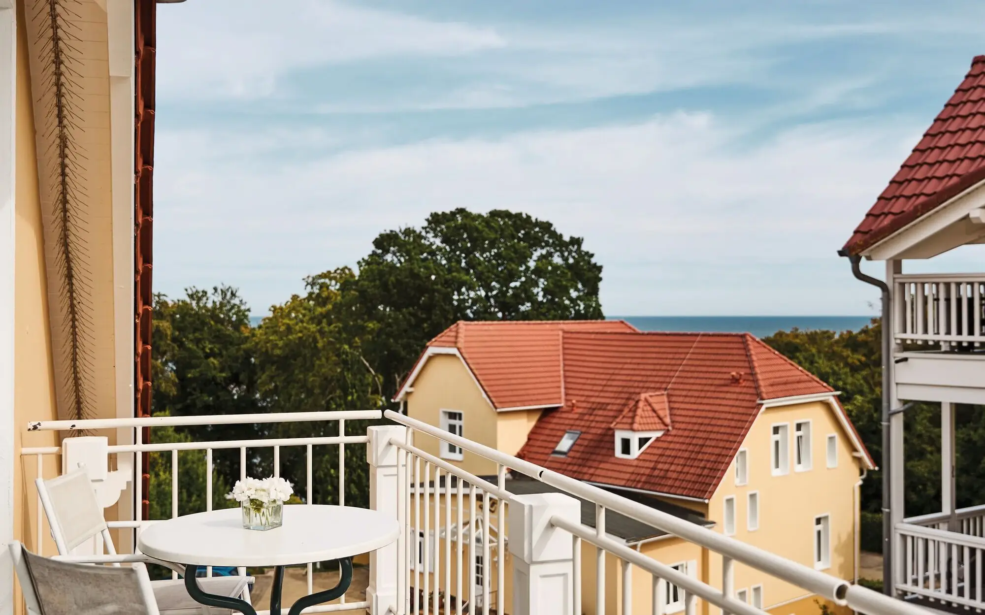 Balkon mit Tisch, umgeben von einem Haus und Bäumen.