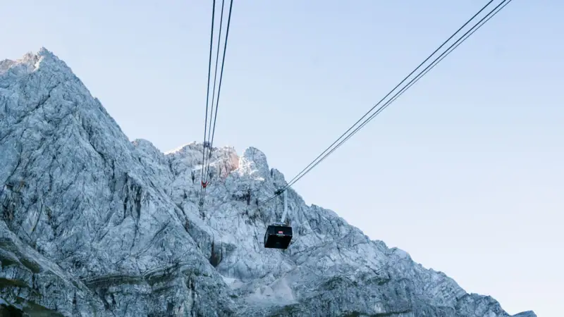 Zugspitzbahn Winter Seilbahn fährt einen Berg hinauf vor klarem Himmel.