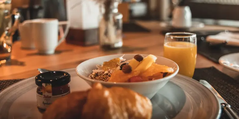 Eine Schüssel mit Müsli und Früchten auf einem Teller mit einem Croissant und Marmelade.