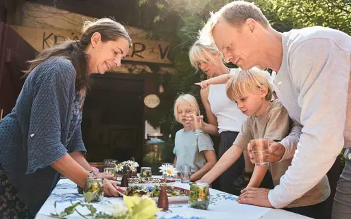 Drei Erwachsene und zwei Kinder stehen draußen um einen Tisch mit Essen herum und lächeln.