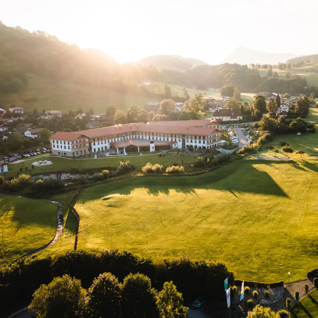 aja Hotel in Ruhpolding Großes grünes Feld mit einem Gebäude und Bäumen im Hintergrund.