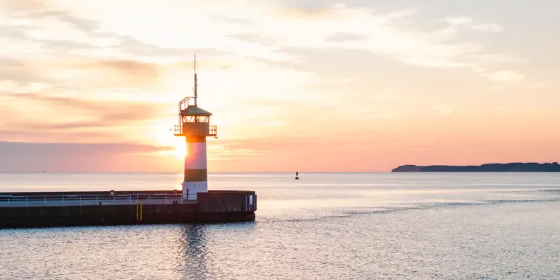 Leuchtturm auf einem Dock inmitten des Ozeans bei Sonnenuntergang.