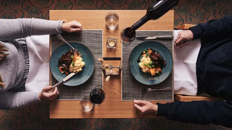 Abendessen Nordperd & Villen Eine Person hält eine Weinflasche und isst.
