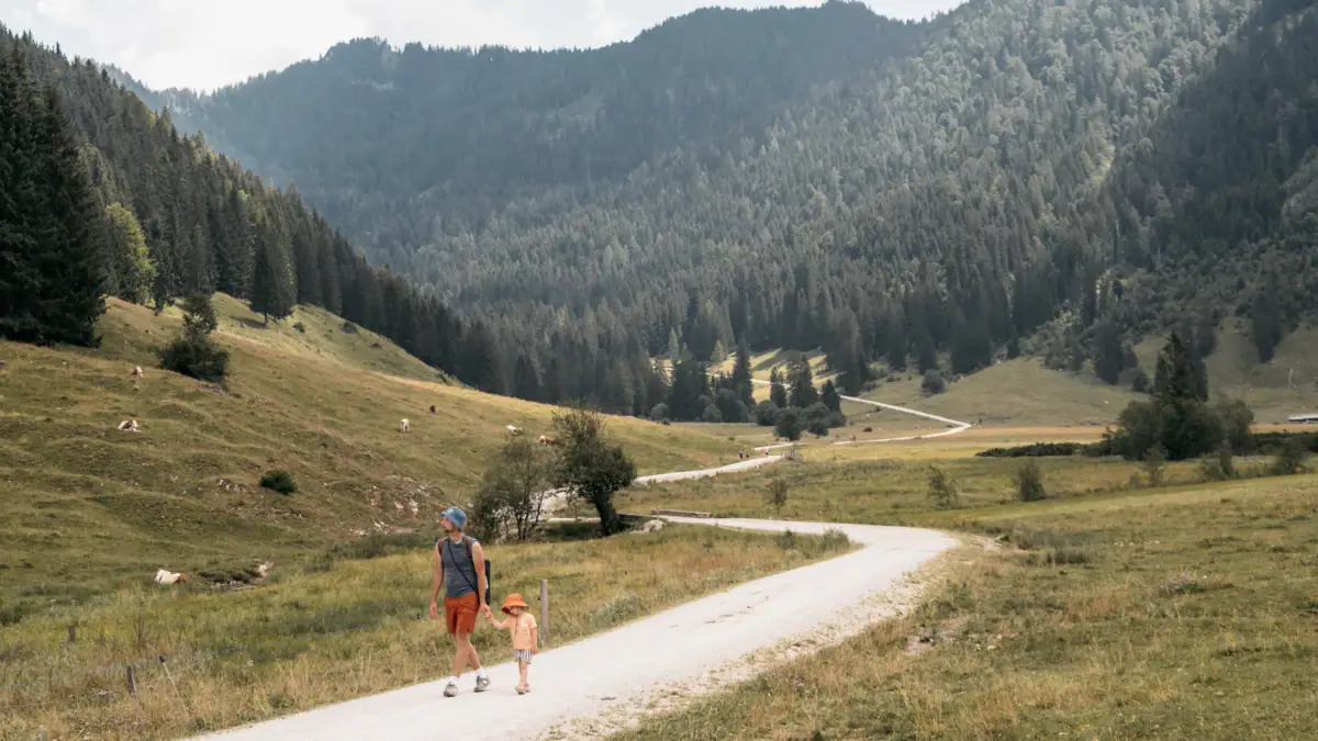 Eine Frau und ein Kind gehen auf einem Feldweg in einer grasbewachsenen Gegend mit Bäumen.