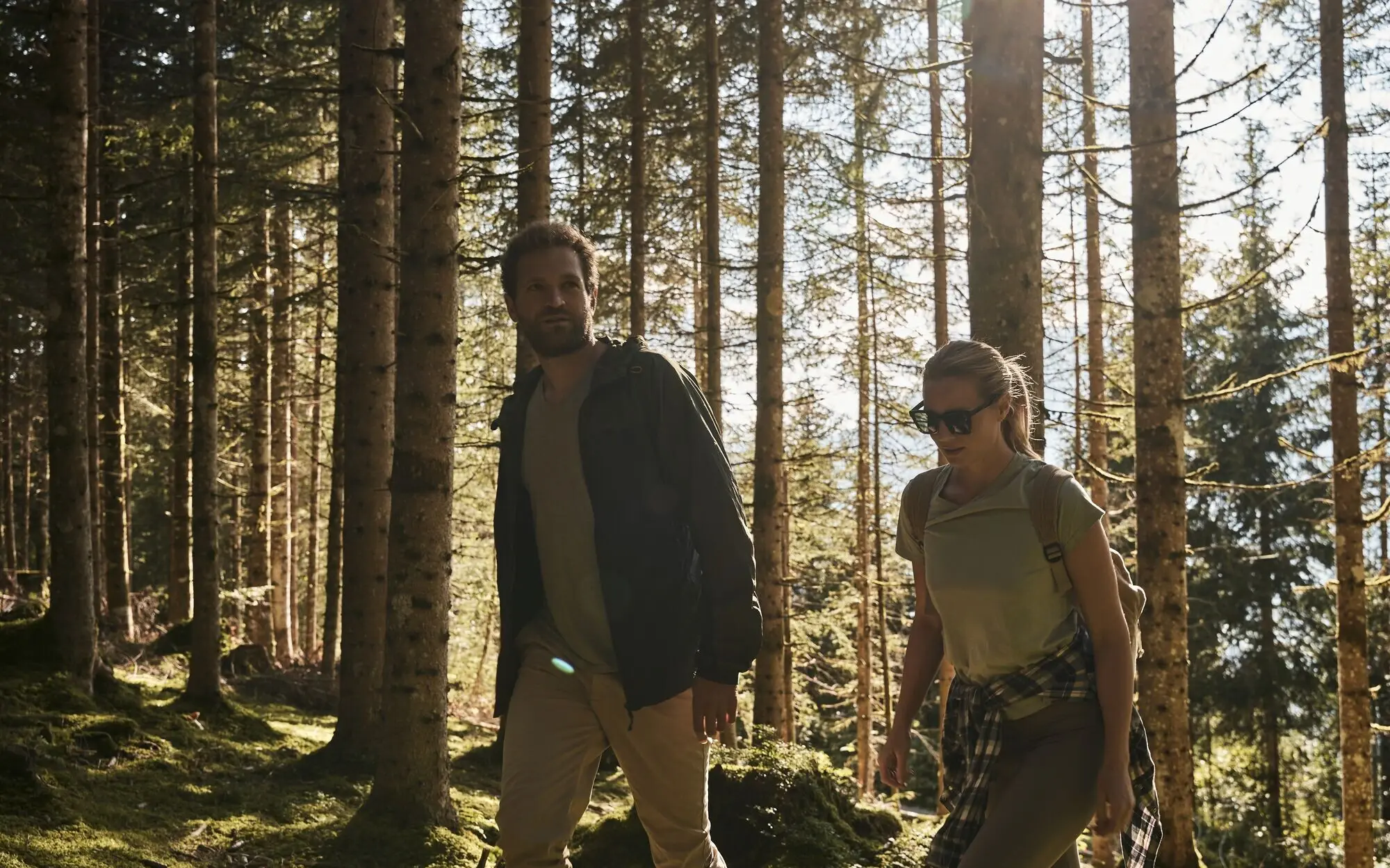 Ein Mann und eine Frau spazieren auf einem Pfad durch ein Feld, im Hintergrund sind Berge zu sehen.