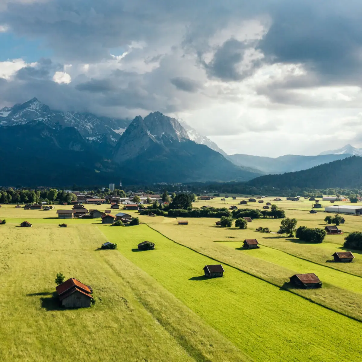Grünes Feld mit Gebäuden und der Zugspitze im Hintergrund