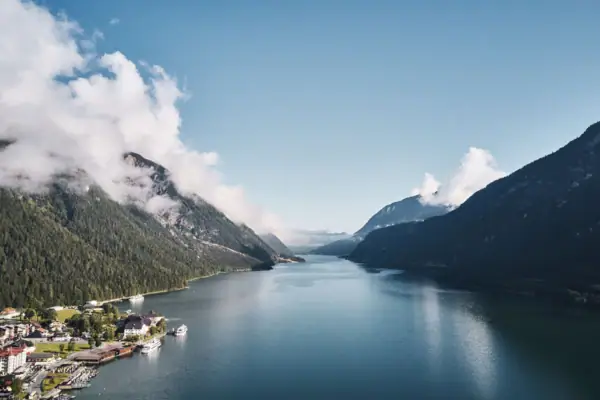 Ein Gewässer mit einem Haus und Bergen im Hintergrund.