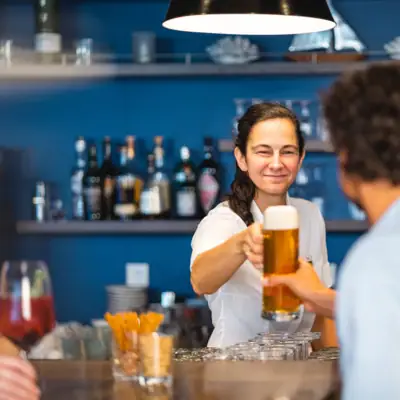 Bar im aja Warnemünde Eine Frau hält ein Glas Bier und steht an der Bar mit einem Gast.