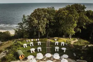 Liegewiese Eine Gruppe von weißen Liegestühlen und Sonnenschirmen auf einer grasbewachsenen Fläche mit Bäumen und Wasser.