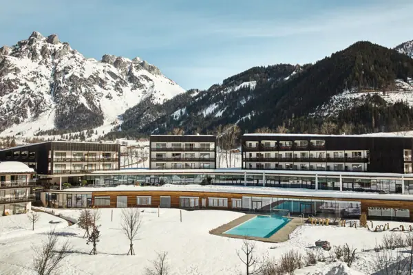 Badewelt im aja Bergresort Werfenweng Das Hotelgebäude mit dem Außenpool im Schnee, umgeben von Bergen.