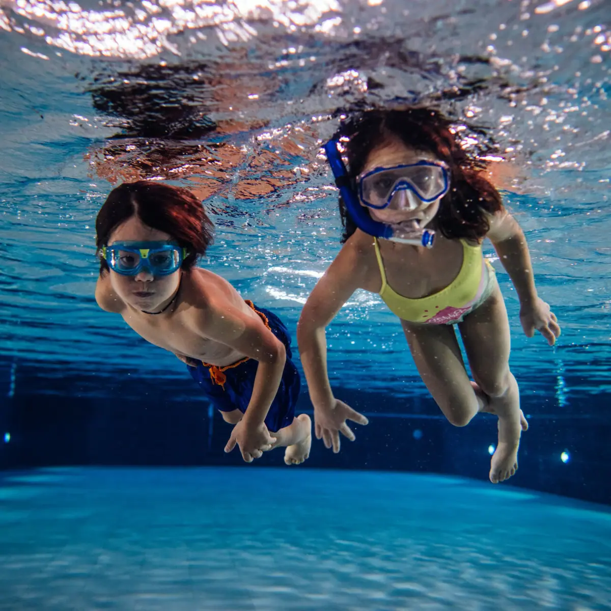 Zwei Kinder schwimmen unter Wasser in einem Schwimmbecken.
