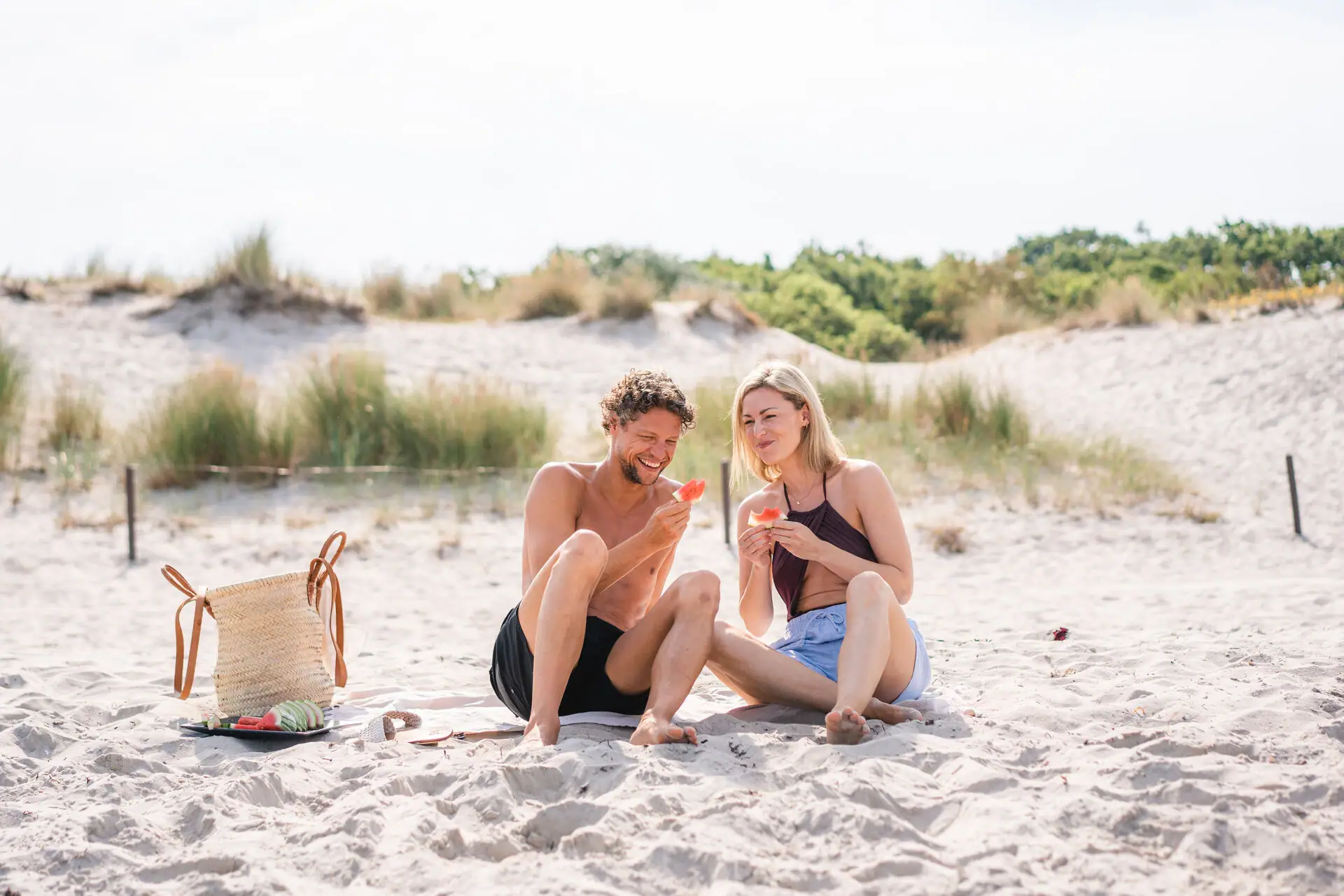 Ein Mann und eine Frau sitzen am Strand und essen Wassermelone.