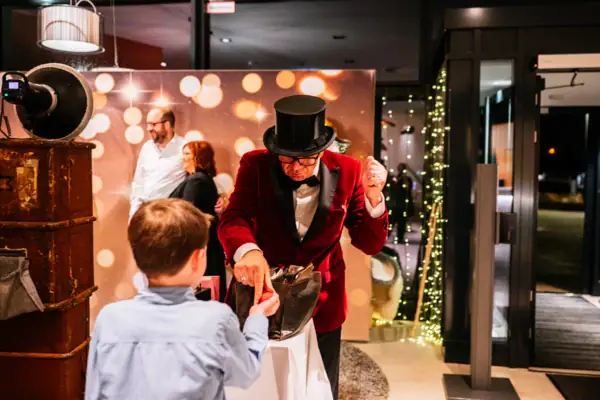 Ein Mann im roten Anzug übergibt einen geknoteten Ballon einem Jungen.