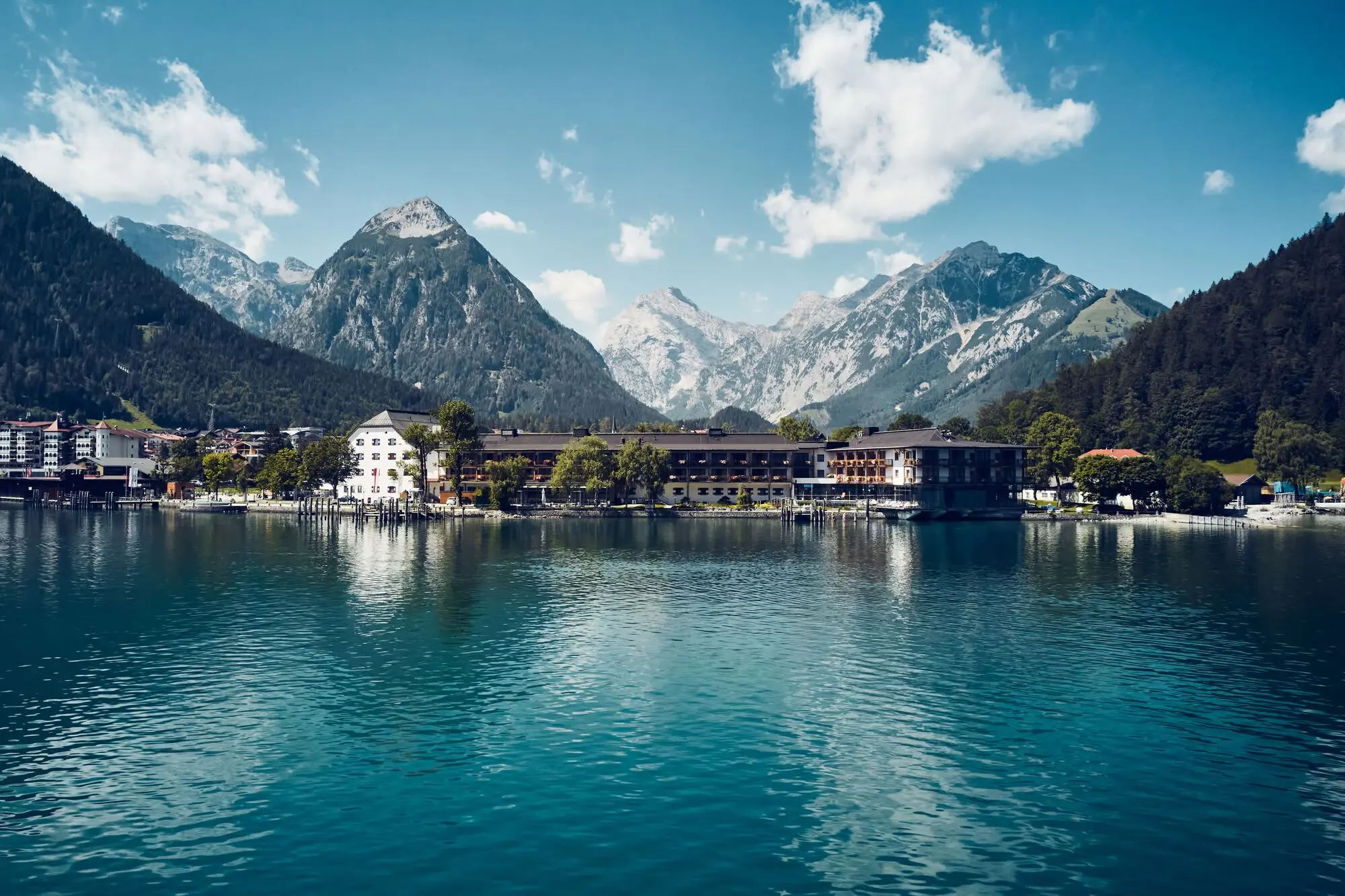 Hotel vor dem Achensee umgeben von Bergen und Bäumen.