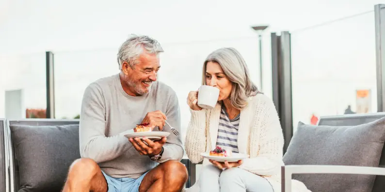 Ein Mann und eine Frau sitzen auf einer Terrasse und trinken Kaffe und essen ein Stück Kuchen.