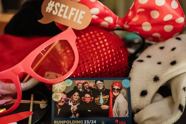 Zubehör zu einer Fotobox auf einem Tisch und ein Foto in der Mitte mit feiernden Menschen.