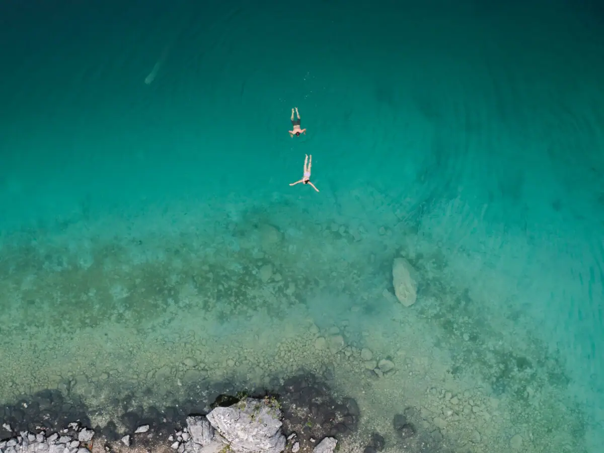 Zwei Personen schwimmen im türkisfarbenen Wasser.