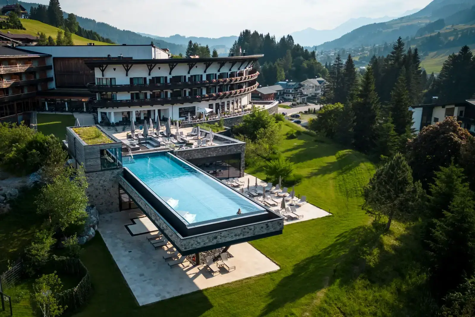 Ifen Hotel Kleinwalsertal Ein Schwimmbecken in einem Gebäude mit einem großen Gebäude und Bäumen im Hintergrund.