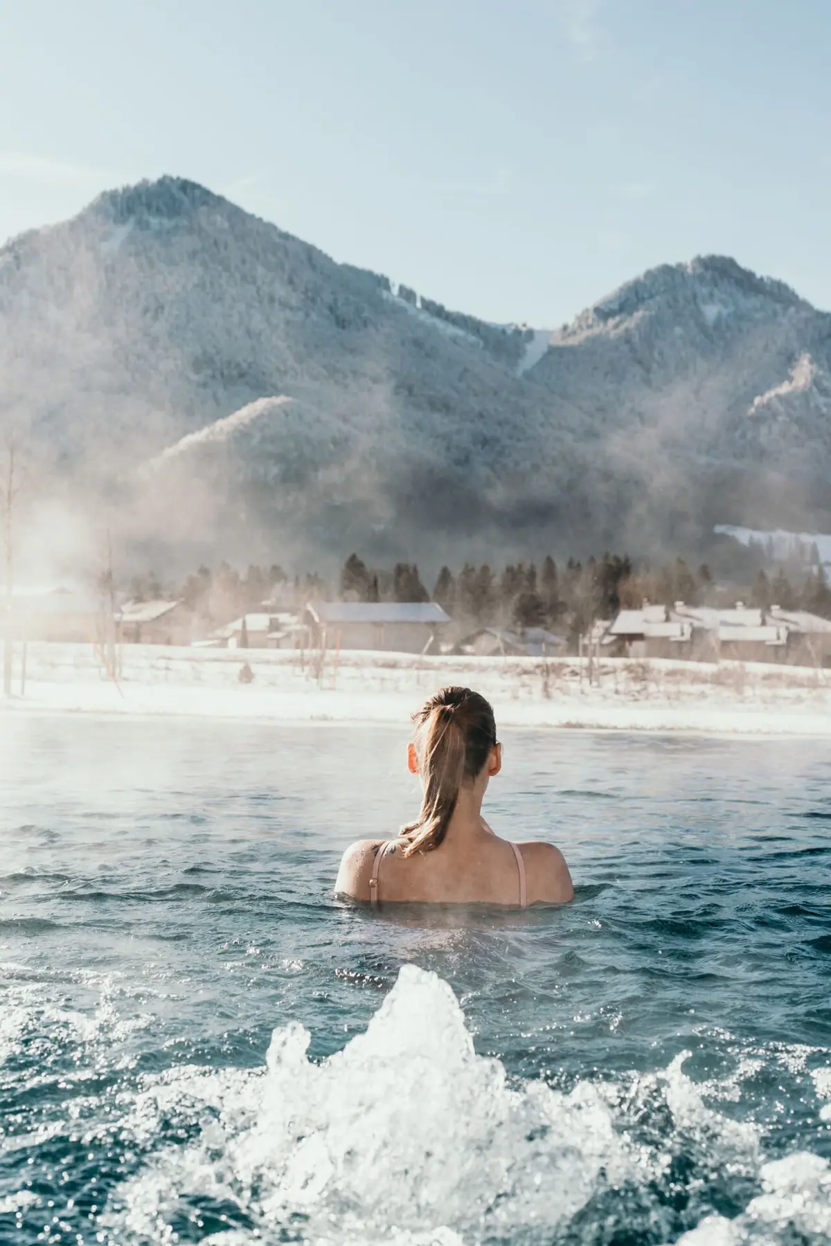 Eine Frau im Außenpool vom aja Hotel Ruhpolding im Winter mit schneebedeckten Bergen im Hintergrund.