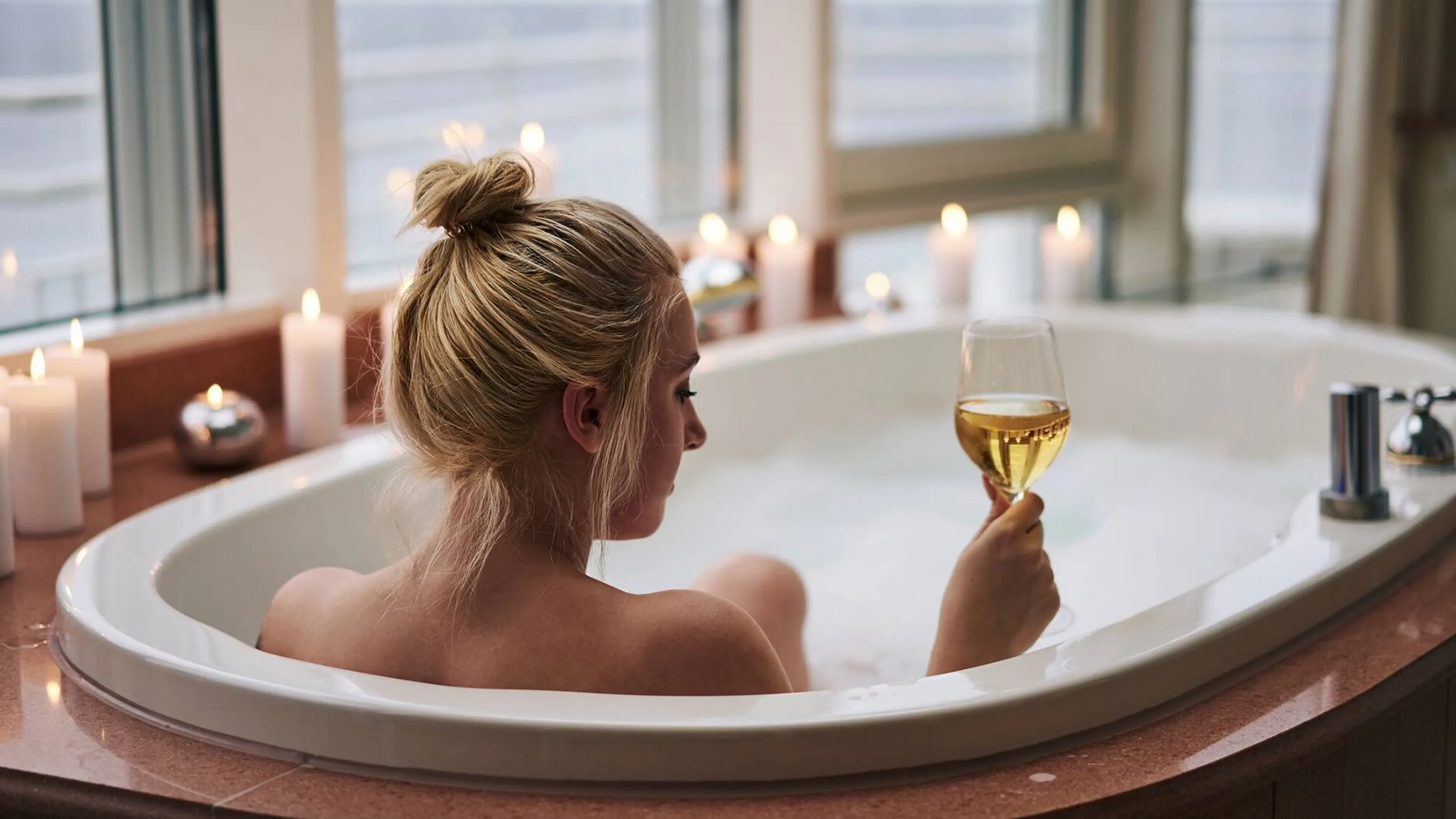 Frau entspannt in einer Badewanne und hält ein Glas Wein in der Hand.