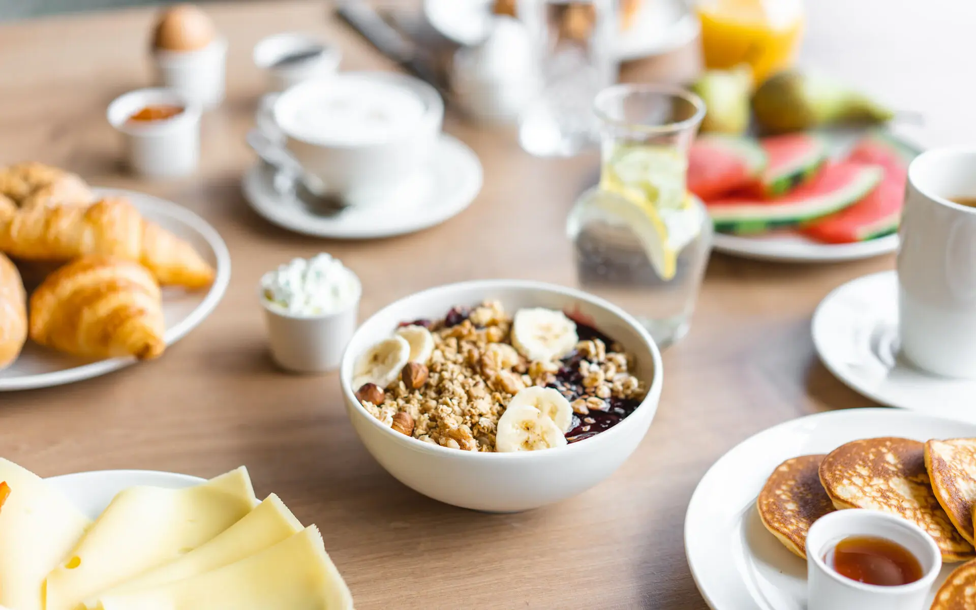 Schüssel mit Müsli, Bananen und Pfannkuchen auf einem Tisch.