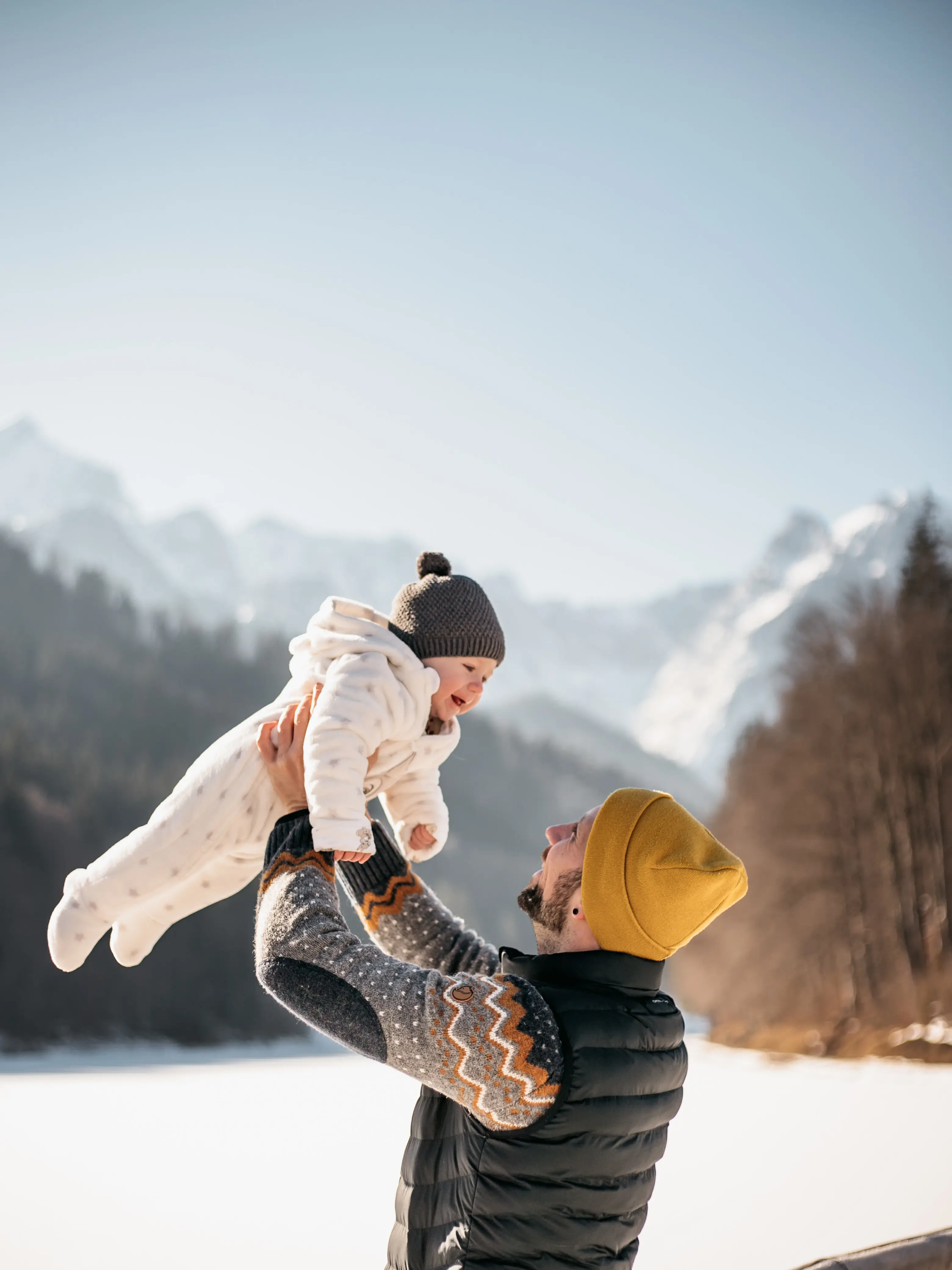 Ein Mann hält ein Baby in der Luft mit der Bergkulisse im Hintergrund