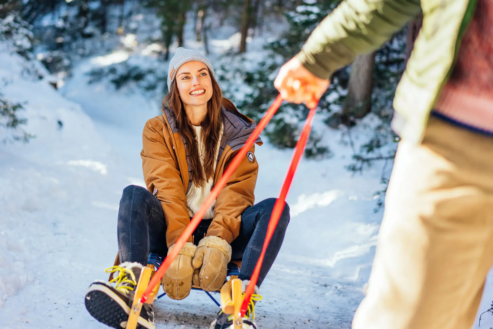 Frau auf einem Schlitten wird von einem Mann durch den Schnee gezogen.