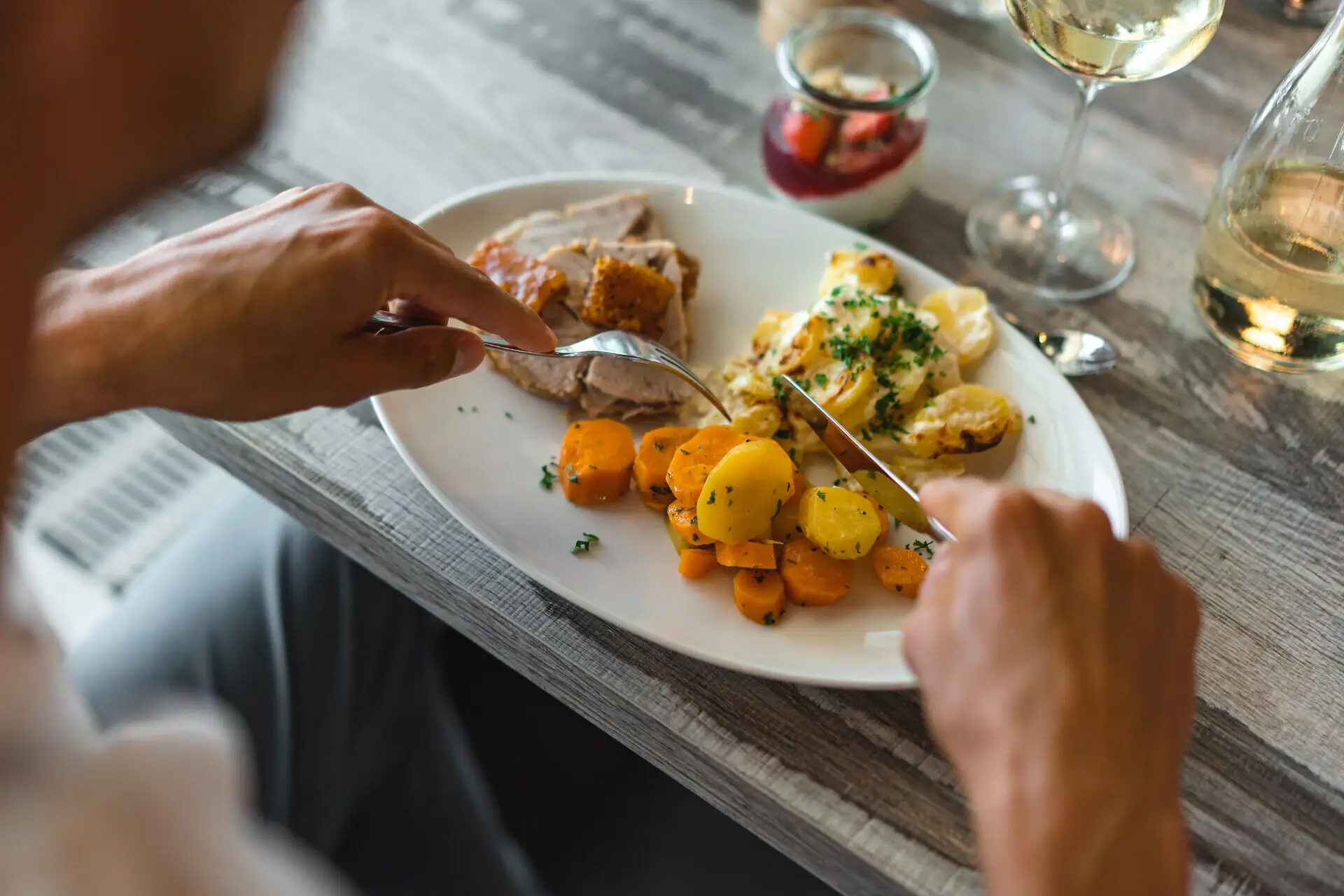 Abendessen im aja Warnemünde Eine Person isst Essen von einem Teller gefüllt mit Karotten, Gratin und Fleisch.