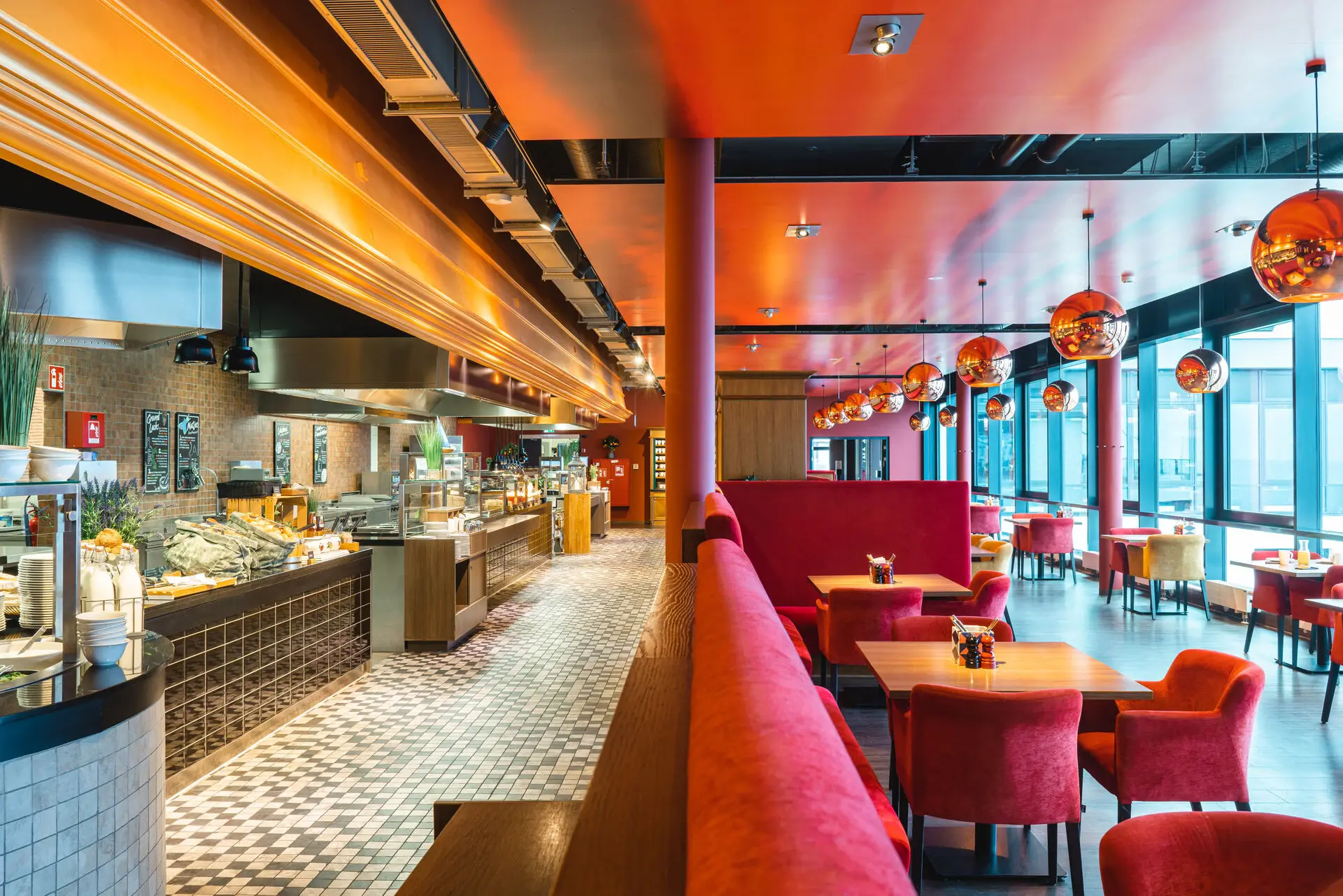 Restaurant-Interieur mit roten Couches und Tischen vor einem Buffet aus verschiedenen Speisen an der Seite