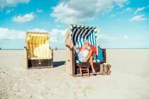 Strandkörbe Travemünde Ein Mann und eine Frau sitzen auf Stühlen am Strand.
