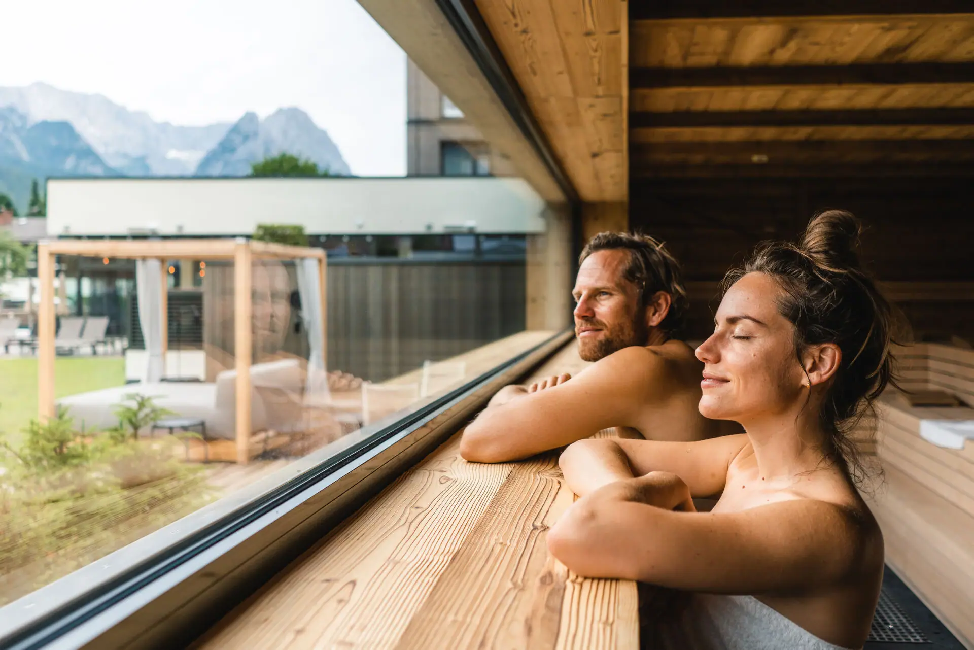 Ein Mann und eine Frau stehen in einer Sauna und lehnen sich an ein Fenster.