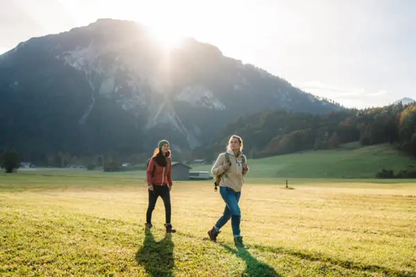 Chiemgau Zwei Frauen gehen in einem Feld mit Bergen im Hintergrund.
