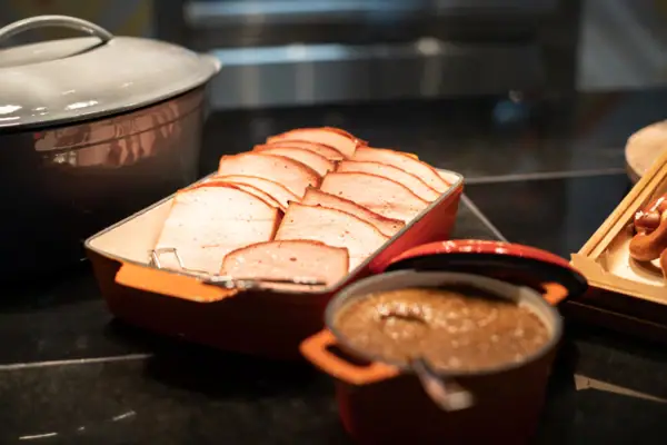 Leberkäse als tägliches Special zum Frühstück Ein Tablett mit geschnittenem Fleisch und eine Schüssel Suppe.