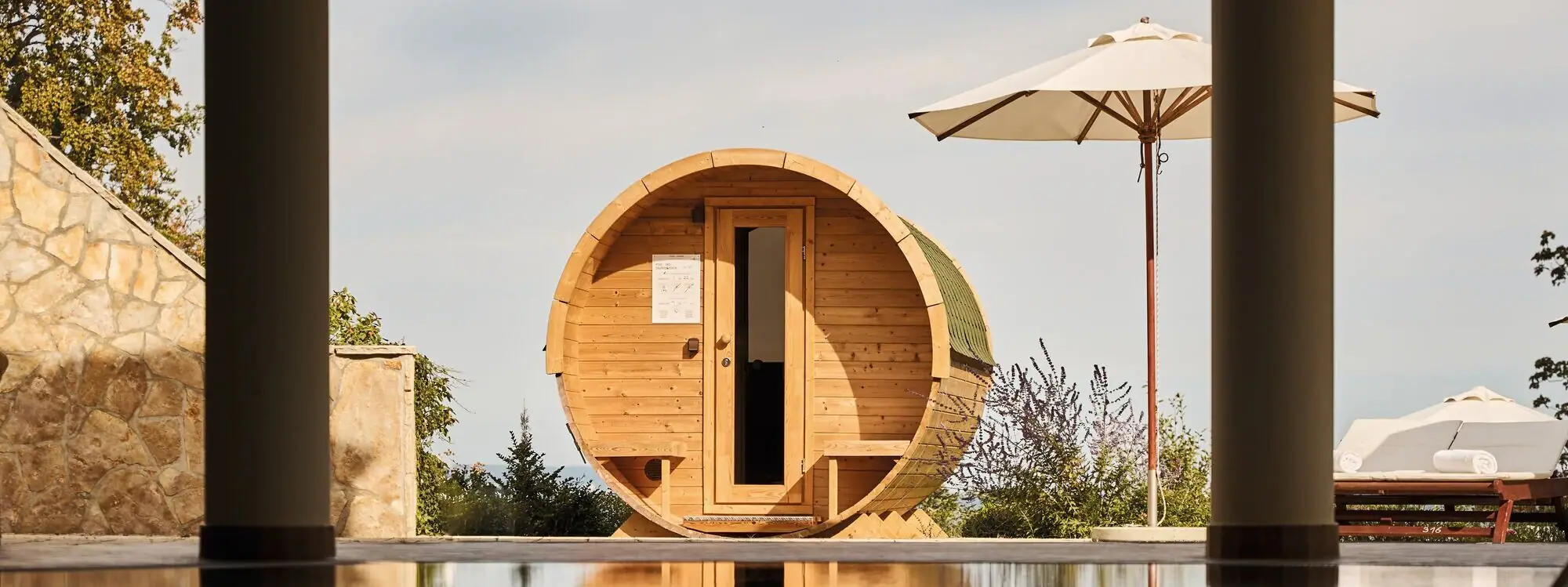 Eine fassförmige Holzsauna neben einem Pool.